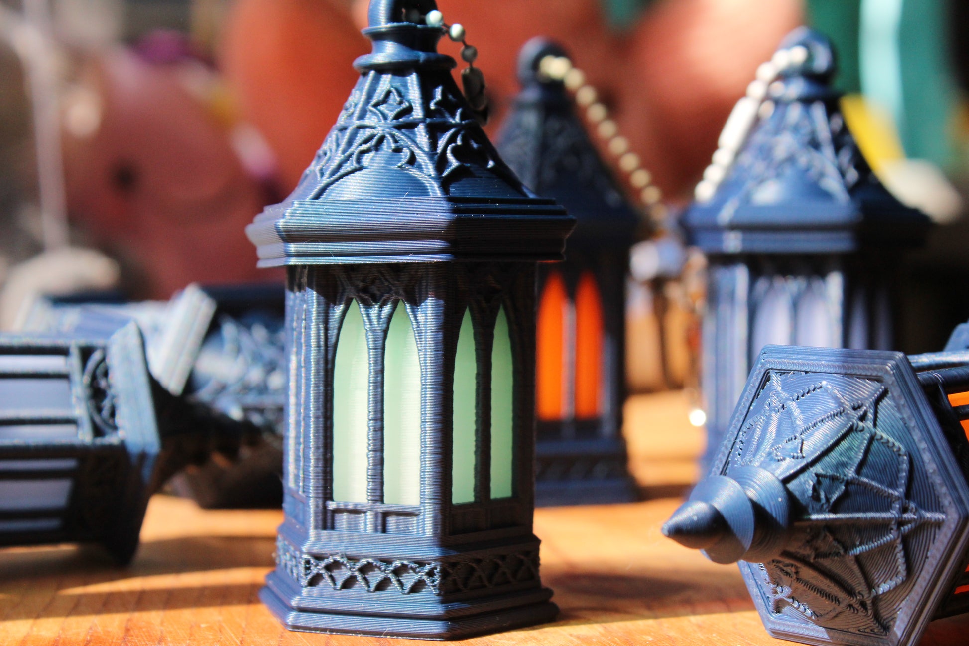 A close-up of a decorative black lantern with green-tinted glass panels, standing on a wooden surface with other similar lanterns blurred in the background.